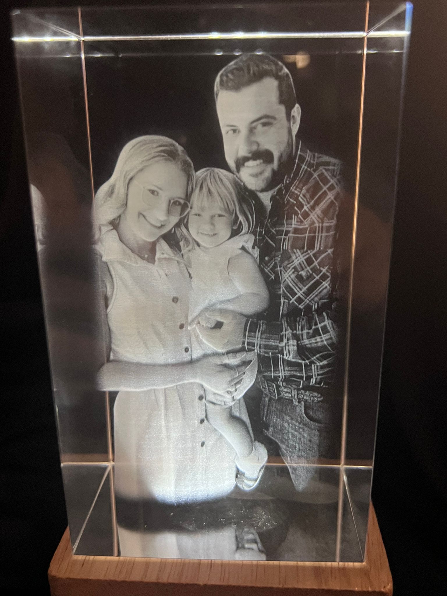Portrait crystal engraving of a family of three — parents with young child — on a warm wooden LED base
